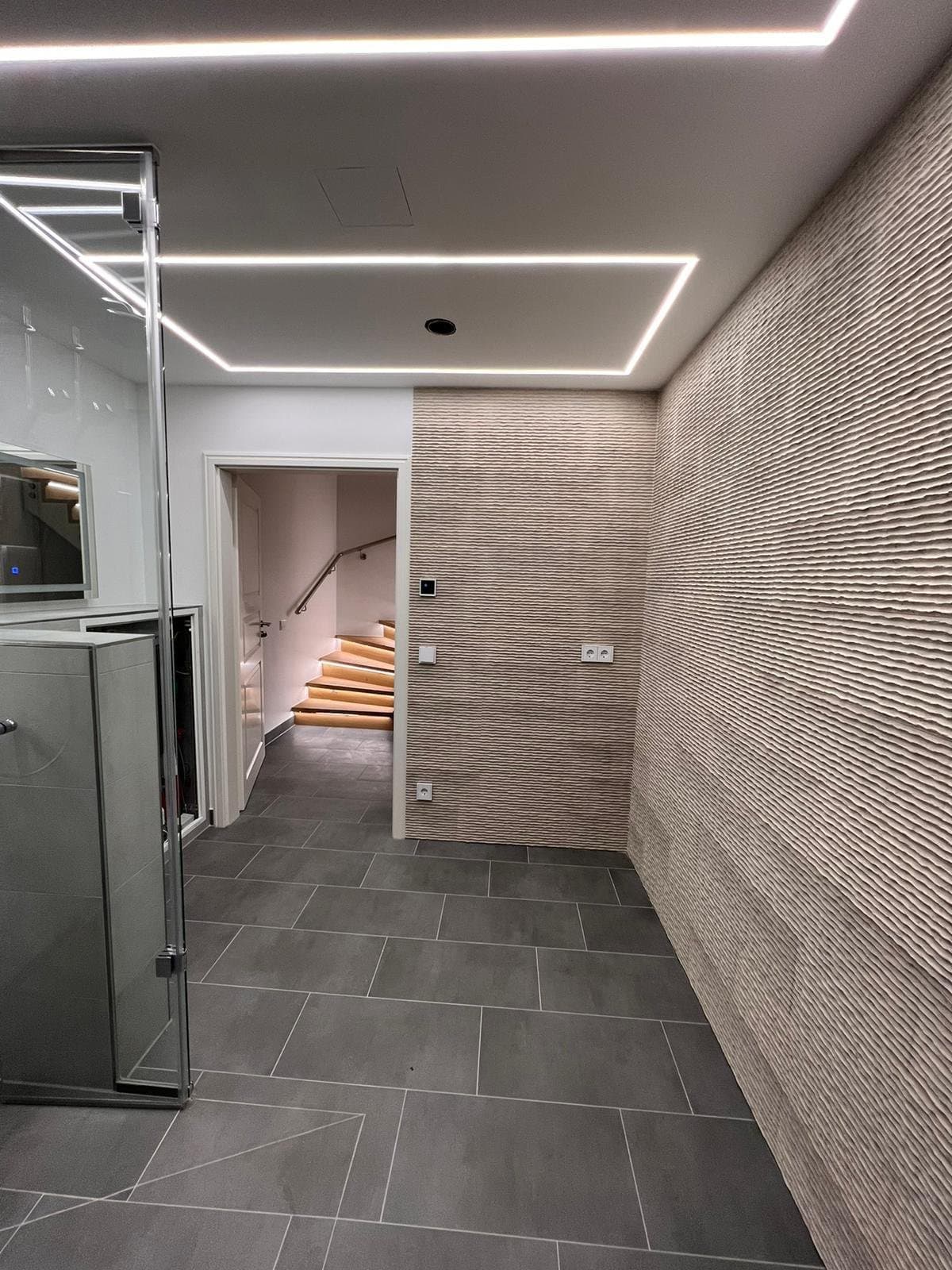 Badezimmer mit LED-Deckenlinien, Glasdusche und strukturierter Wandverkleidung