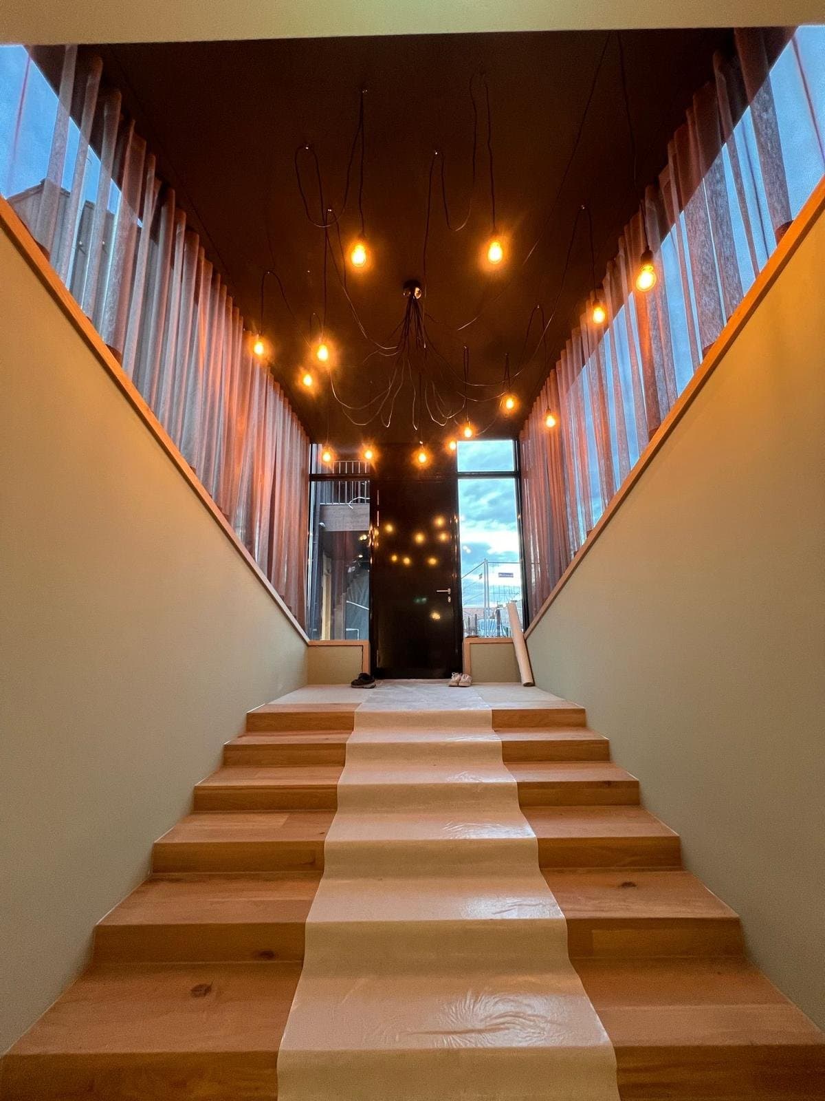 Breite Holztreppe unter einer dunklen Decke mit zahlreichen hängenden Glühbirnen-Pendelleuchten