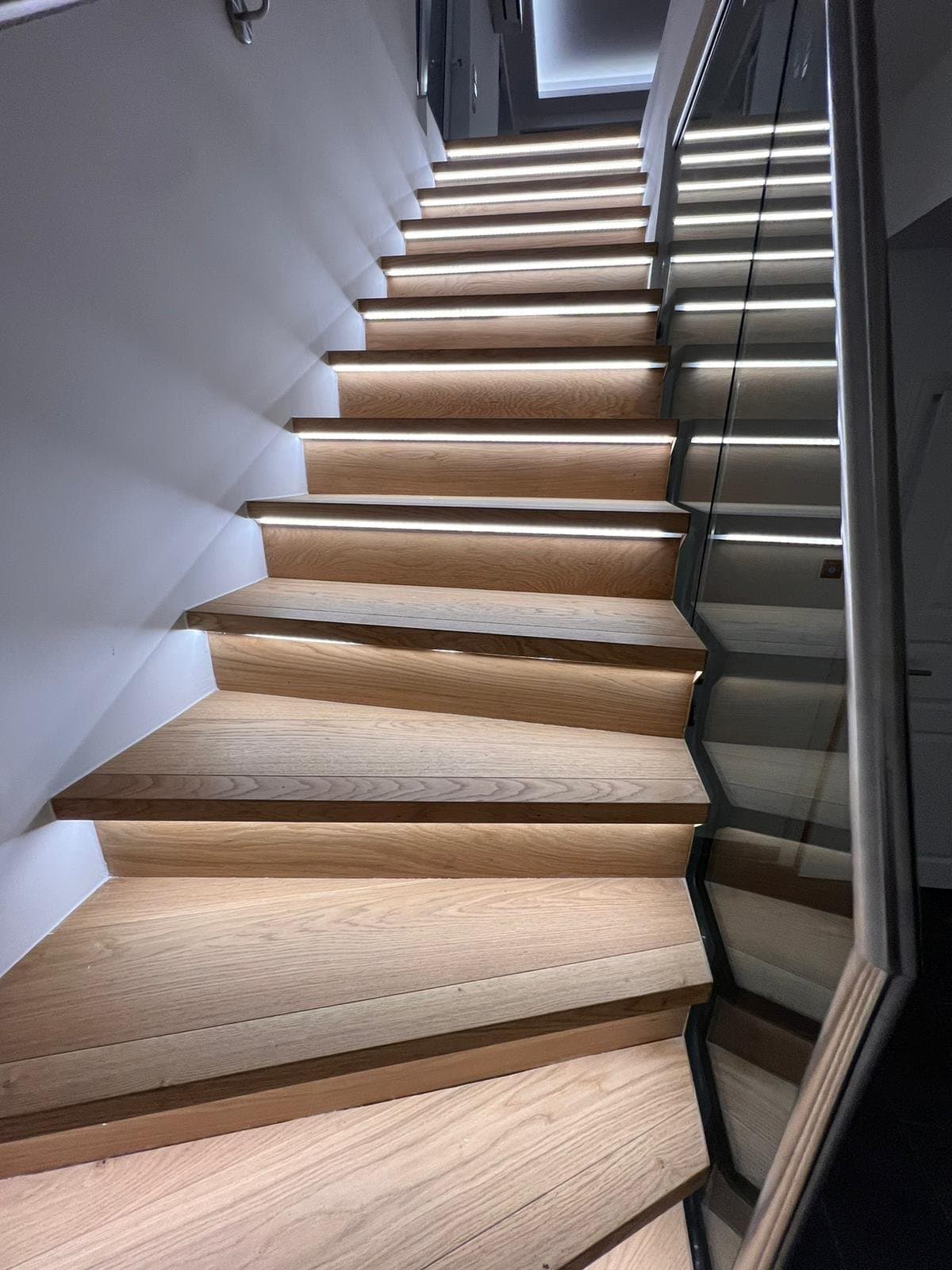 Holztreppe mit in jede Stufe integrierten LED-Lichtleisten und Glasgeländer